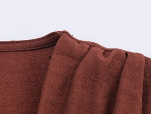 Macro view of textured brick red crepe fabric and stitching details on V-neck dress