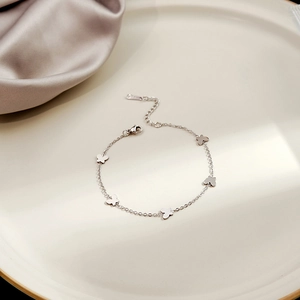 Detailed view of silver butterfly chain bracelet on a ceramic plate with satin