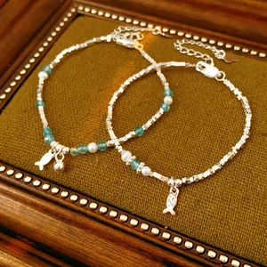 Detailed shot of silver beaded bracelets with pearls and fish charms on green velvet
