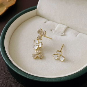 Detail of asymmetric gold clover flower earrings with white shell and zircon inlay