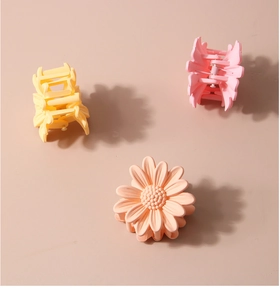 Three daisy-shaped matte hair claws in yellow, pink, and peach on a soft beige surface