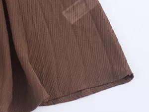 Dettaglio macro dell'abito in maglia color caffè con trama plissé fine e orlo cucito con cura