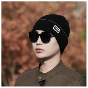 Detail of black ribbed knit beanie with fashion patch on blurred autumn background