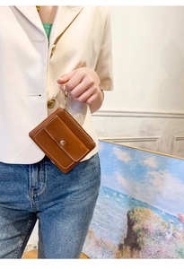 Close-up of a brown leather mini wallet with white stitching and gold keychain held by hand
