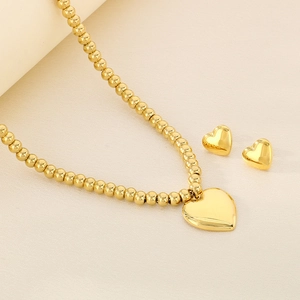 Close-up of gold heart pendant necklace and stud earrings jewelry set on beige fabric