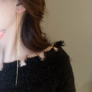 Macro close-up of elegant gold tassel earrings with zircon studs and delicate shimmering chains