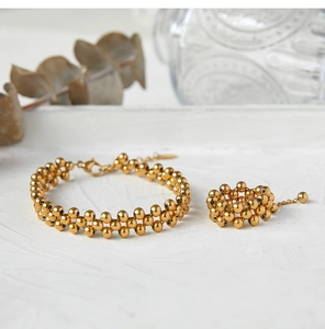 Detail of a gold multi-layer beaded bracelet and ring set on a white textured surface