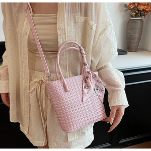 Pink woven bucket bag with silk scarf detail and crossbody strap shown on a model