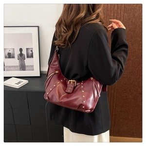 Detail of burgundy leather tote featuring golden studs and buckle on the shoulder bag