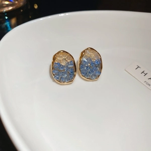 Detailed close-up of vintage blue floral earrings with gold trim on a white plate
