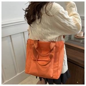 Detail of the orange tote bag with front pocket and nylon texture worn on shoulder