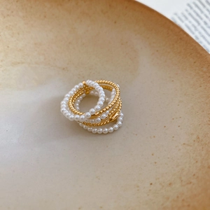 Detail of multi-layer pearl and gold bead rings on beige ceramic tray with soft lighting