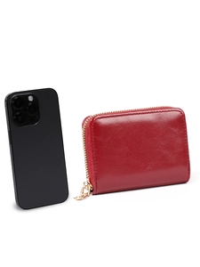 Size comparison of a red glossy leather card holder with gold zipper next to a smartphone