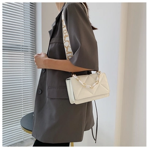 Close-up of white quilted crossbody bag with wide strap and decorative thick chain detail