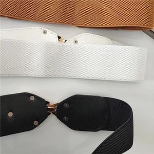 Close-up of three elastic belts in brown, white, and black with golden metal buckles