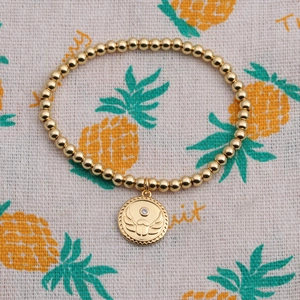 Detail of 18K gold plated beaded bracelet with Egyptian scarab wing pendant on linen background