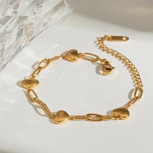Detail view of gold paperclip chain bracelet with four polished heart charms and lobster clasp
