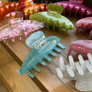 Close-up of glittery and floral acrylic hair claws with seven-tooth design on a wood shelf