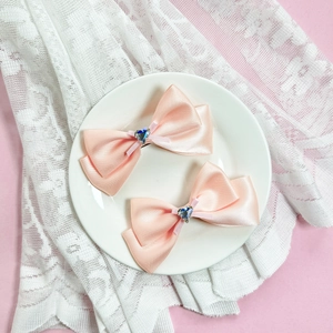 Détail de barrettes noeud en satin rose avec gemme en forme de coeur et dentelle