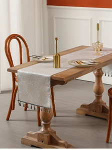 Detail of silver gray jacquard table runner with elegant tassels on a wooden dining table