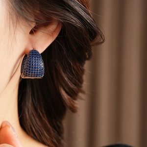 Macro view of C-shaped silver earrings featuring pave-set dark blue cubic zirconia stones