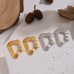 Detailed view of textured gold and silver irregular earrings on a minimalist stone plate