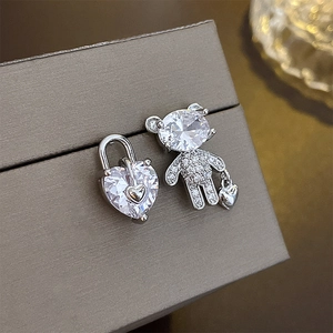 Macro detail of asymmetric silver teddy bear and heart lock earrings with cubic zirconia
