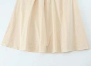 Close-up of the beige poplin midi dress showing the textured hemline and draped fabric detail