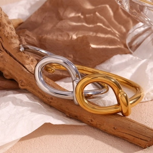 Detail of twisted knot open bangles in gold and silver finish on natural wood