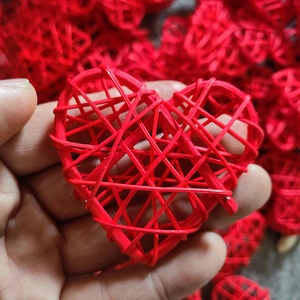 Close-up of a hand holding a red woven heart ornament made of natural rattan fibers