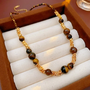 Détail macro de perles d'oeil de tigre et chaîne dorée dans un écrin à bijoux brun