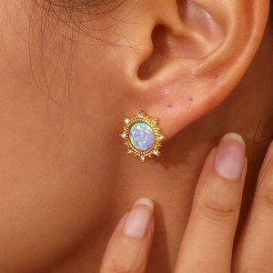 Detailed view of sunburst gold earring with opal stone and crystals on female ear