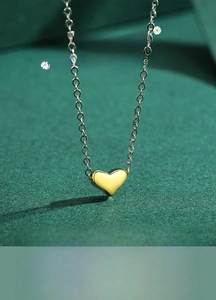 Close-up of a polished gold 3D heart pendant on a fine silver-colored chain necklace