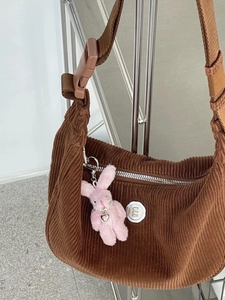 Detail of a brown corduroy shoulder bag featuring a cute pink plush bunny keychain charm