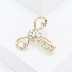 Detailed close-up of a gold uterus brooch with clear rhinestones and faux pearls