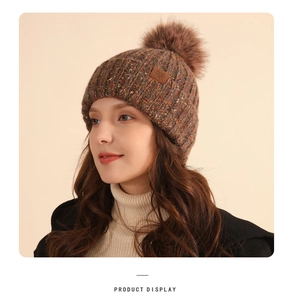 Detail of mixed-color knit beanie featuring a faux fur pompom and snowflake leather patch