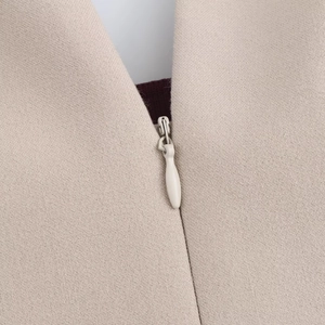 Dettaglio macro della cerniera invisibile bianca su un abito beige in maglia a coste