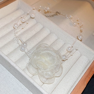 Macro detail of triple-layer pearl choker with elegant white lace mesh flower on jewelry tray