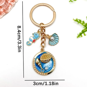 Golden ocean keychain with blue enamel seahorse, shell, and pearl on white background