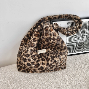 Detail of leopard print faux fur tote bag with canvas logo label on textured white surface