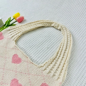 Detail of beige knit tote bag with pink heart pattern and thick woven handles
