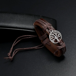 Detail of vintage brown leather bracelet with tree of life charm on black background