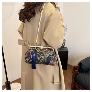 Detail of vintage navy floral handbag with pearl chain and tassel worn with trench coat