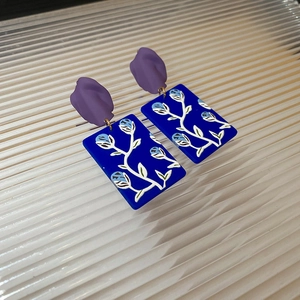 Detail of artistic resin drop earrings with blue floral patterns and purple matte accents