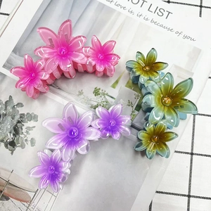 Detailed view of three gradient floral hair claws in pink, purple, and green on a magazine