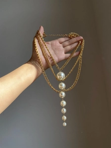 Detailed view of triple-layered golden chain necklace with vertical pearl pendant drops