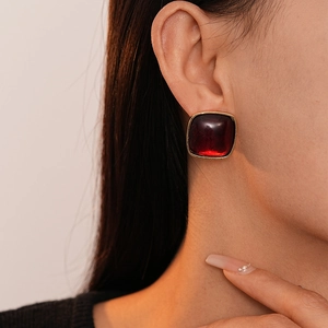 Close-up of square resin stud earring in dark red with golden frame worn on earlobe
