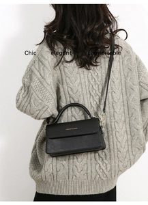 Dettaglio di una borsa a tracolla in pelle nera chic con finiture dorate su maglia