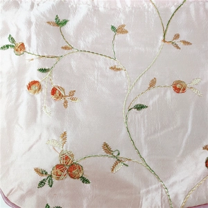 Close-up of silk fabric with floral embroidery featuring green leaves and orange berries