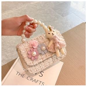 Detail of pink tweed girl's bag featuring pearl handle and cute plush rabbit charm